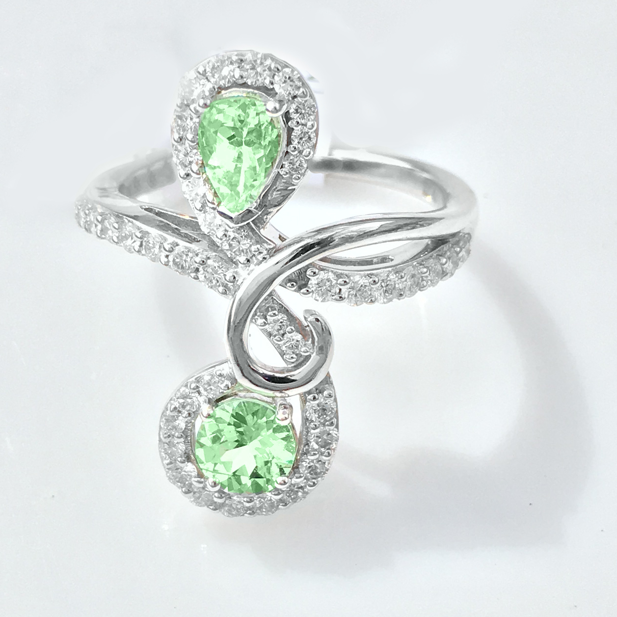 White gold ring holding two pear-shaped mint garnets, each in a diamond halo, on a swirling split band