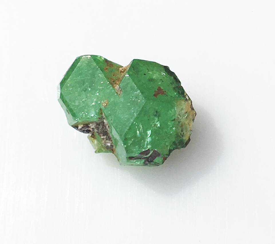 A rough green grossular garnet crystal on a plain background