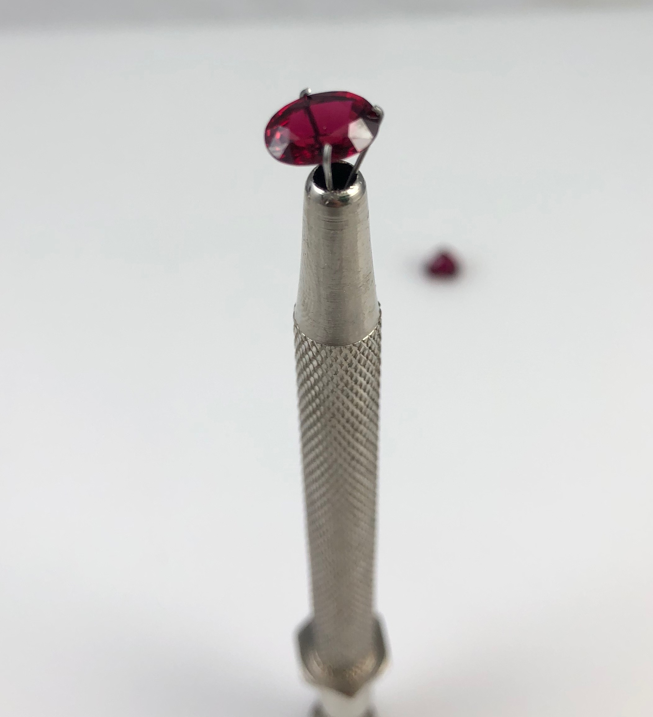 A ruby held in a setter's tool, seen from the side so the pavilion is visible