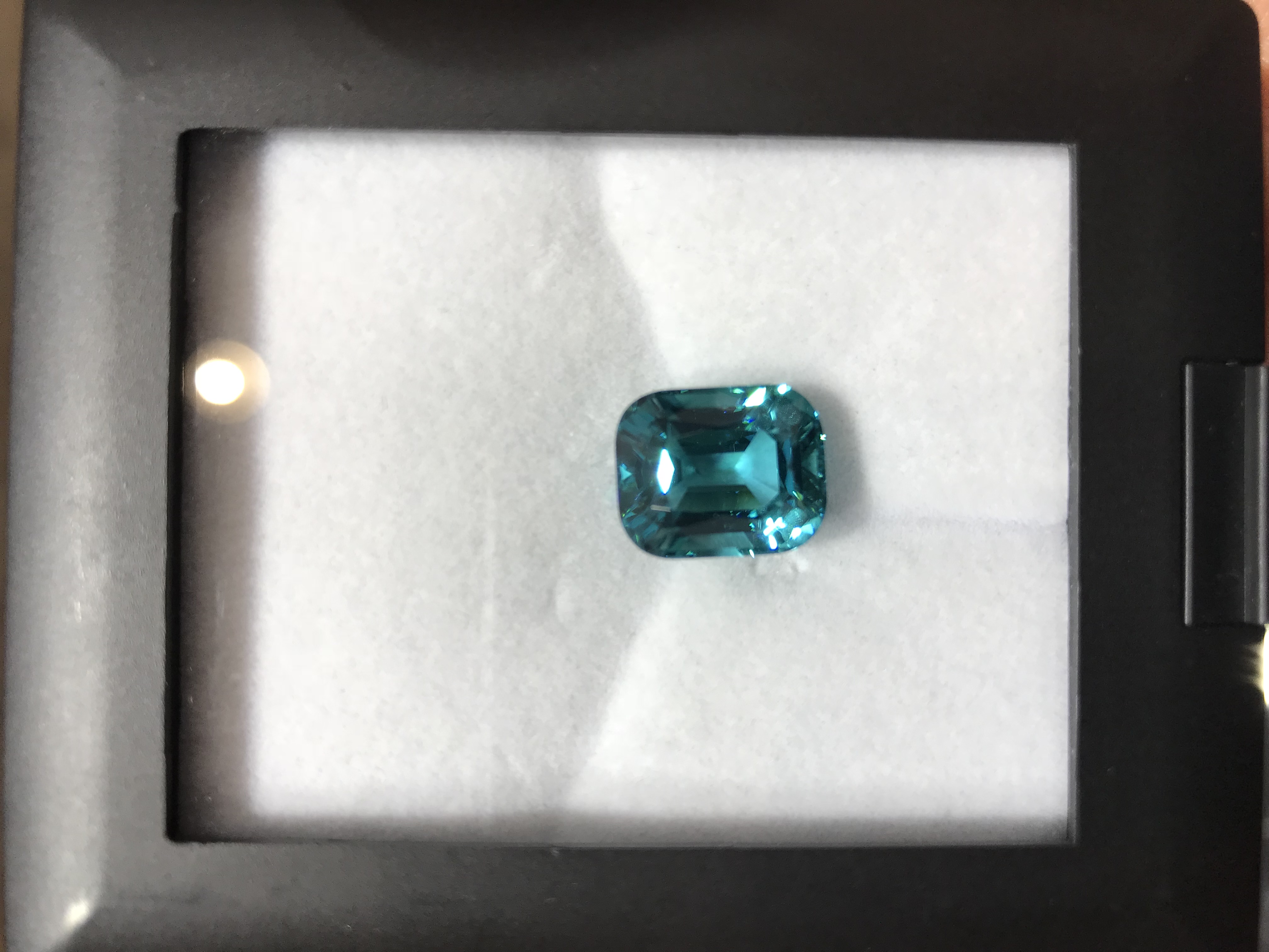 A cushion-cut blue-green tourmaline displayed in a gem box