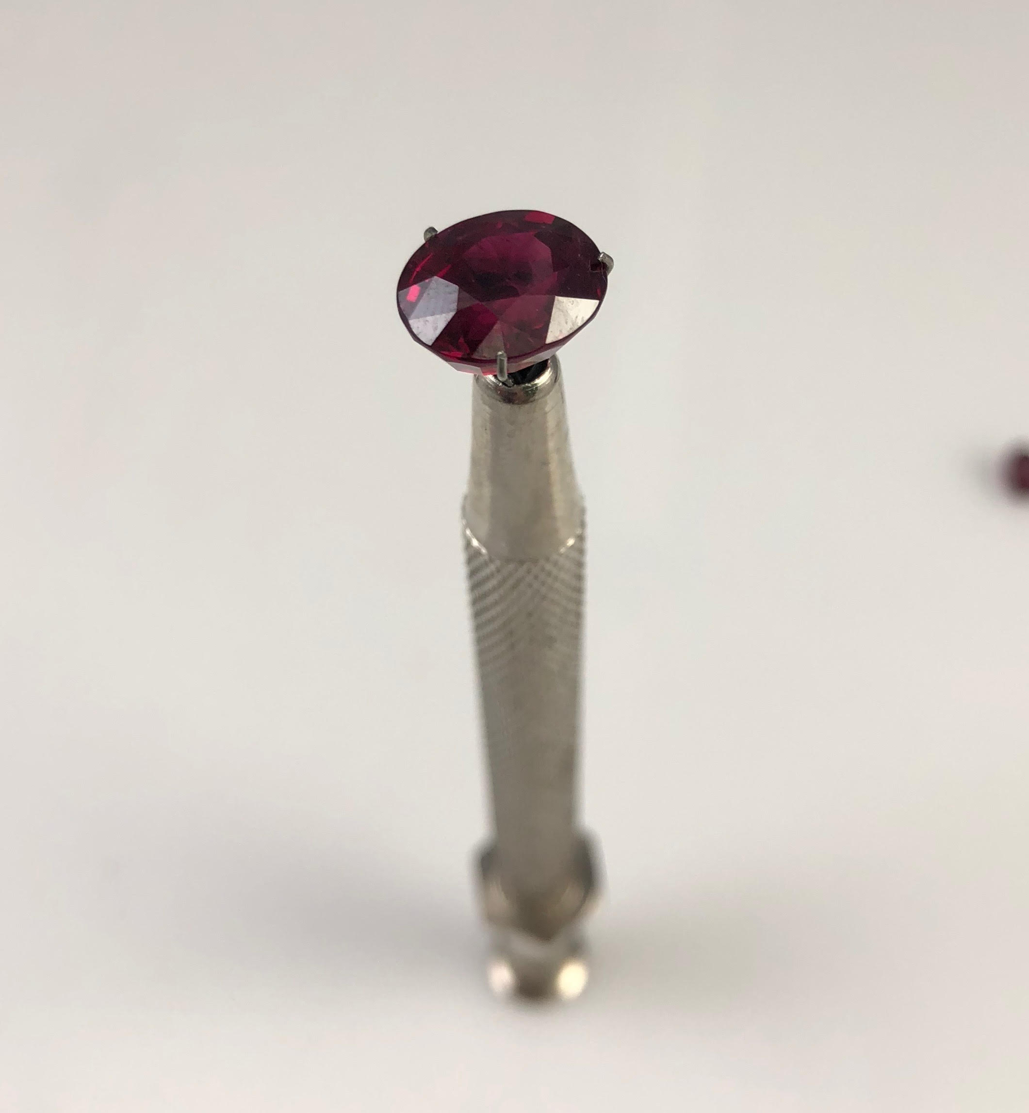 An oval ruby held upright in a gem holder for inspection