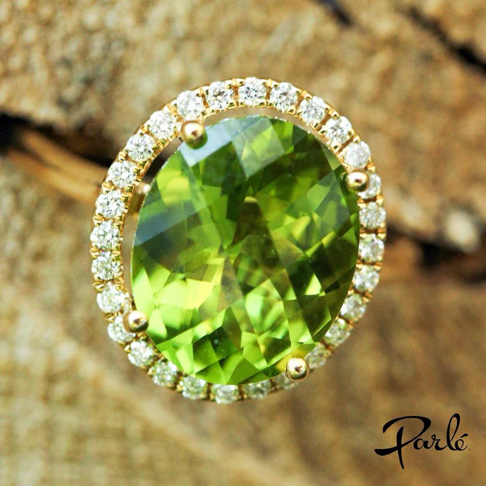 Round peridot ring in yellow gold with a halo of diamonds, photographed on bark