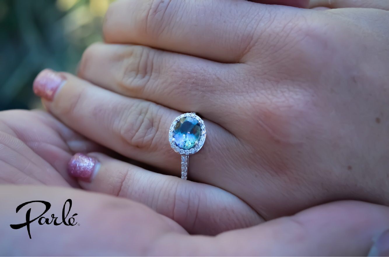 A hand wearing an oval tanzanite ring with a diamond halo