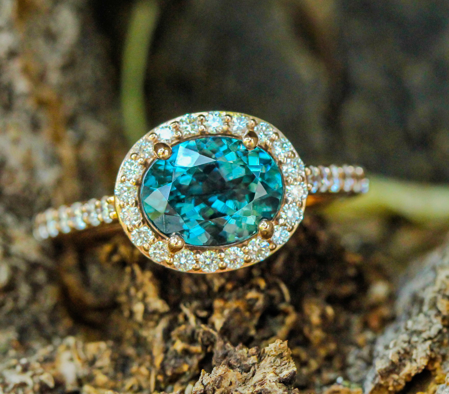 Blue-green spinel ring with a diamond halo in rose gold, photographed on tree bark