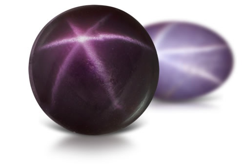 Two star spinel cabochons, one dark purple and one lavender, each showing a six-rayed star