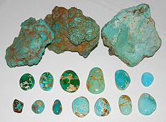 Rough turquoise pieces displayed above two rows of the polished cabochons cut from them, ranging from green to blue