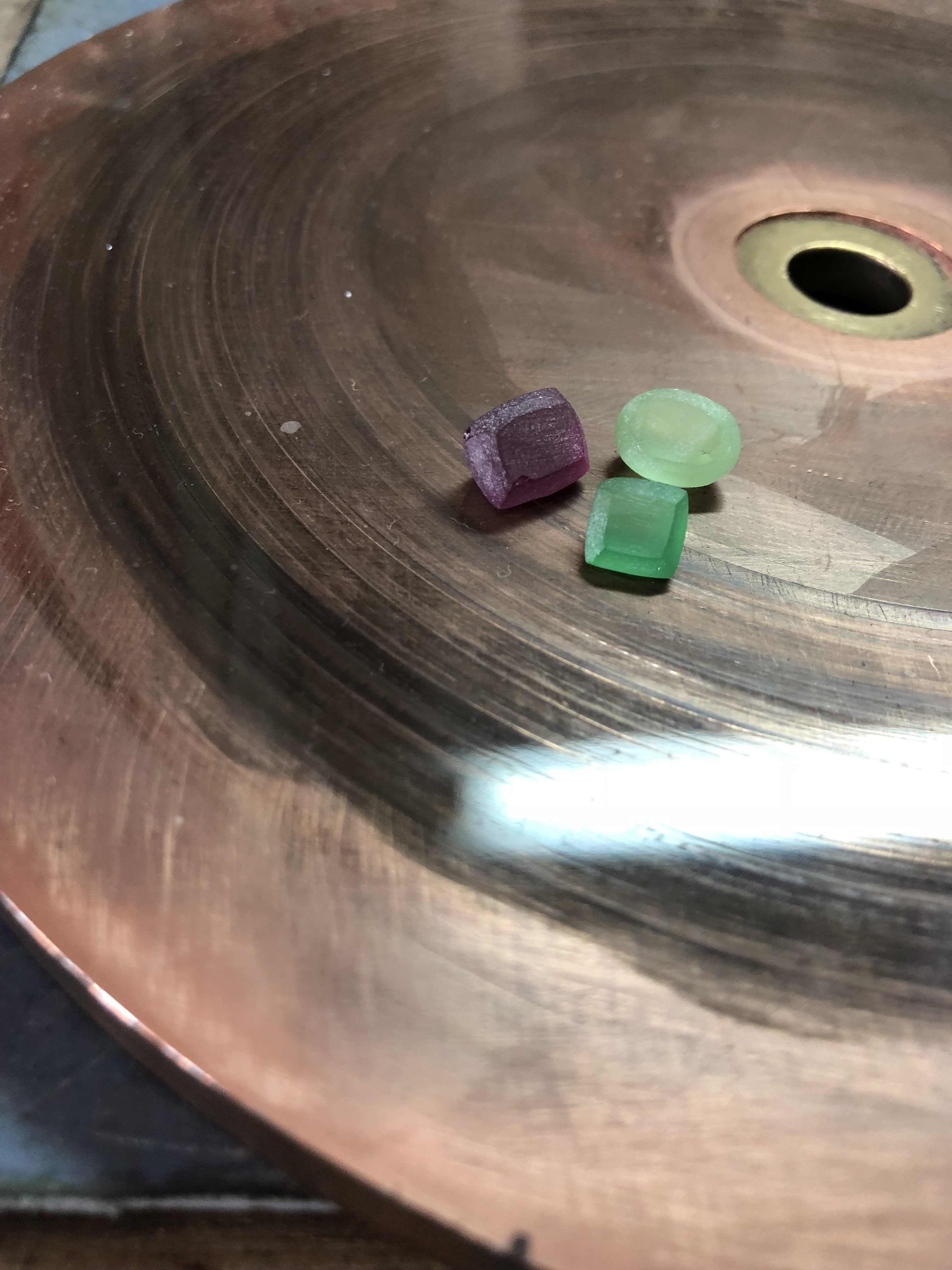 A small purple stone and a small green stone resting on a lapidary polishing wheel